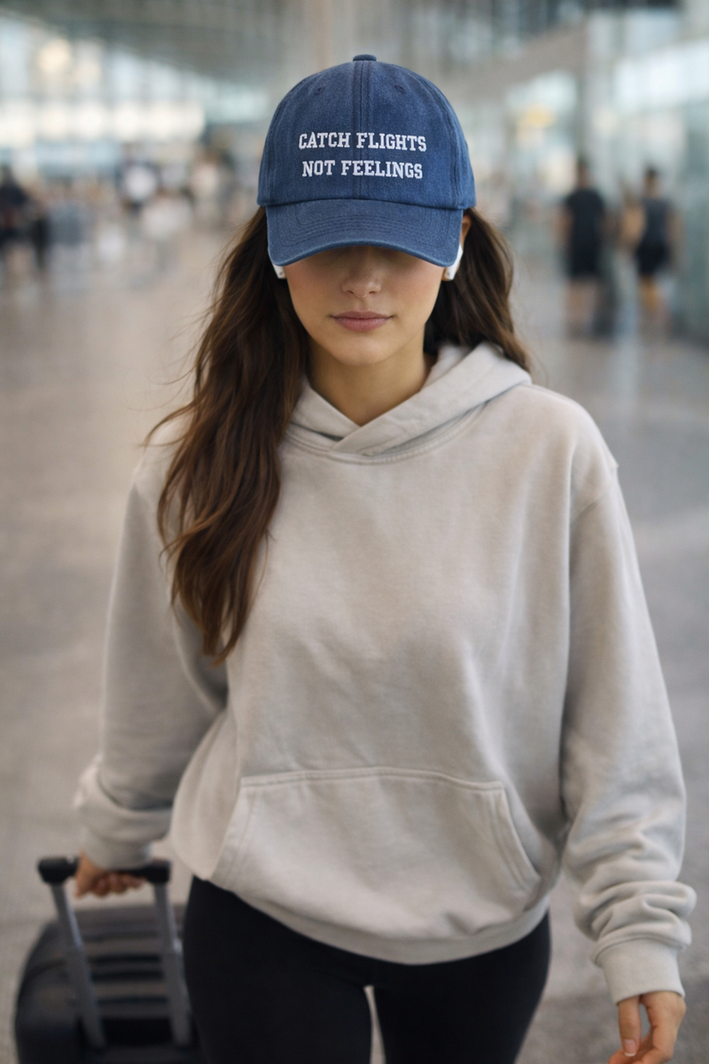 Woman wearing a blue cap with text and a gray hoodie, walking through an airport.